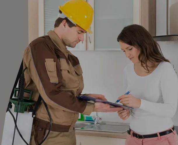 Brantford pest control technician in a yellow hard hat reviewing a treatment plan on a clipboard with a homeowner in her kitchen